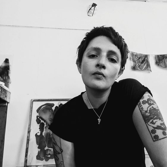 A black and white portrait of a person with dark short cropped hair and arm tattoos.