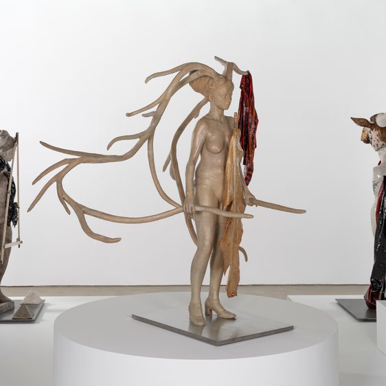 Three figurative sculptures on plinths inside a gallery.