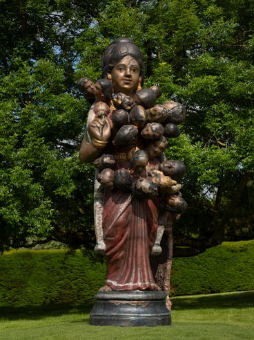 A sculpture of a giant Indian golu doll, with additional heads emerging from it's shoulders and torso, displayed outdoors.