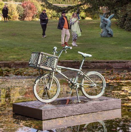 A bronze bicycle sculpture displayed on a plinth in the middle of a pond.