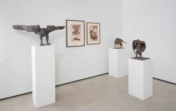 An exhibition of plaster sculptures of animals displayed on plinths, and framed drawings.