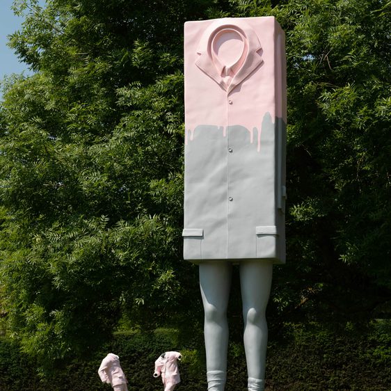 A pink and grey box on legs wearing a suit, two headless sculptures wearing pink suits in the background