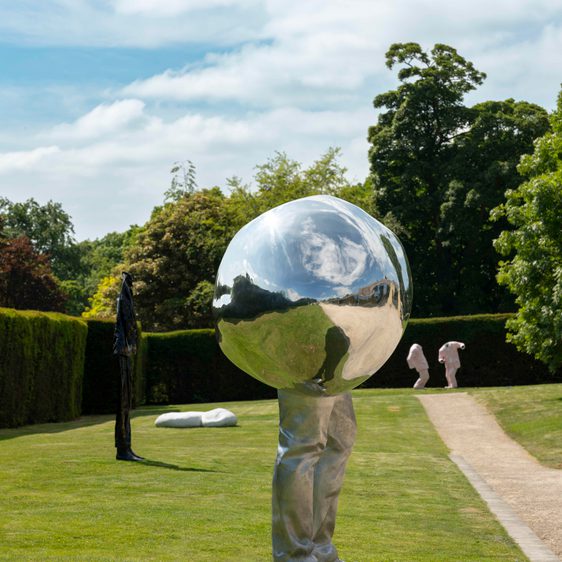 A silver sculpture with legs on the lawn and more sculptures in the background.