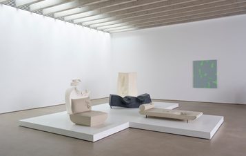 Five sculptures on a white plinth in a gallery and a canvas hung on the wall.