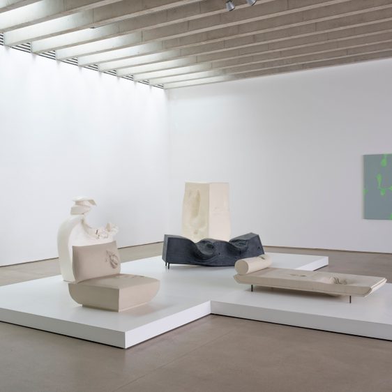 Five sculptures on a white plinth in a gallery and a canvas hung on the wall.