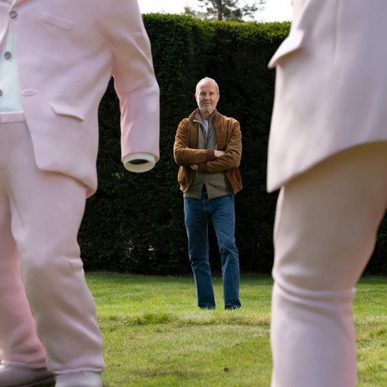 Man in the background, stood in between two pink sculptures of dancing suits