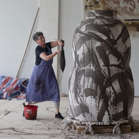 Woman painting a larger than life sized ceramic vase with big paintbrush