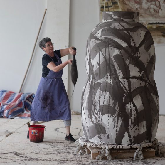 Woman painting a larger than life sized ceramic vase with big paintbrush