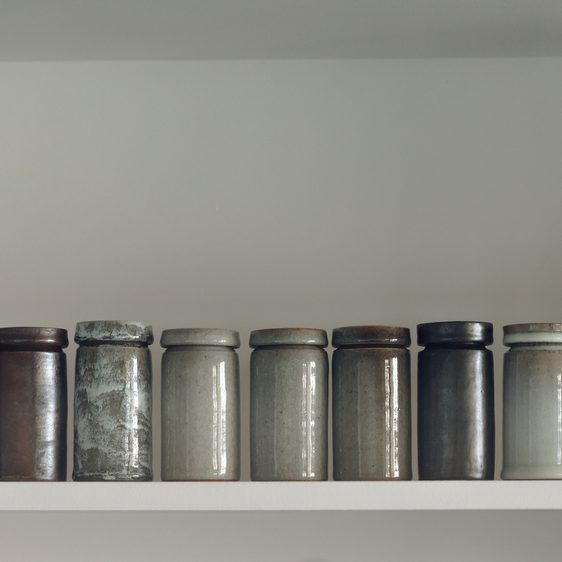 Nine lidded ceramic pots on a shelf