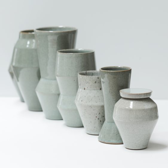Six green-toned ceramic vases and lidded pots in a row