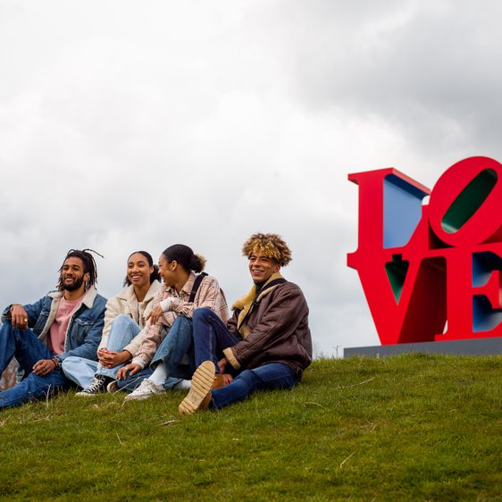 Four friends chatting in front of a red sculpture that reads LOVE