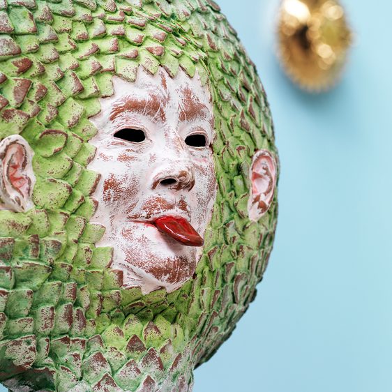 A green round sculpture of a face, sticking its tongue out