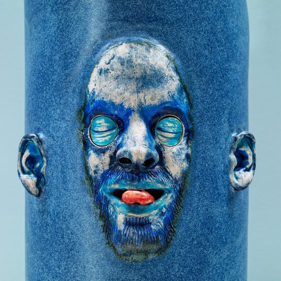 Close up of a blue sculpture of a face with their eyes closed and sticking out their tongue