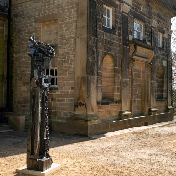 Black wooden sculpture outside a stone building.