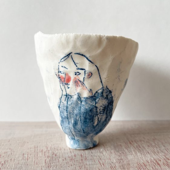 A small ceramic cup with an illustration of a person with rosy cheeks.