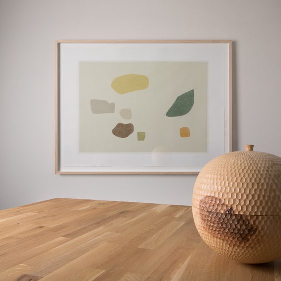 A framed print hung on a wall and a carved wooden vessel in the foreground.
