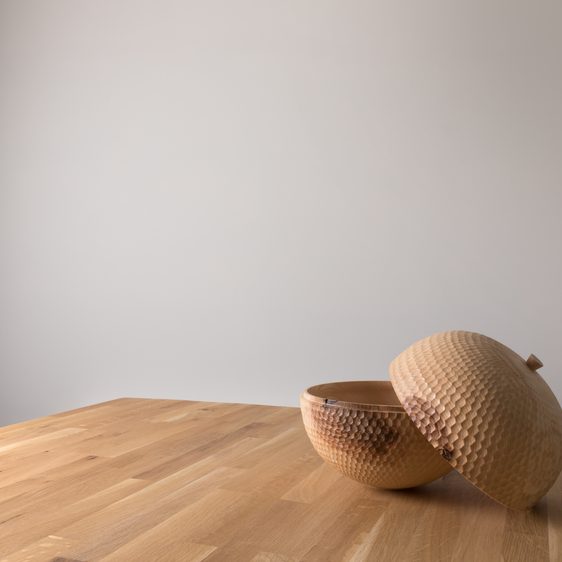 A carved wooden vessel with its lid off, on a wooden surface