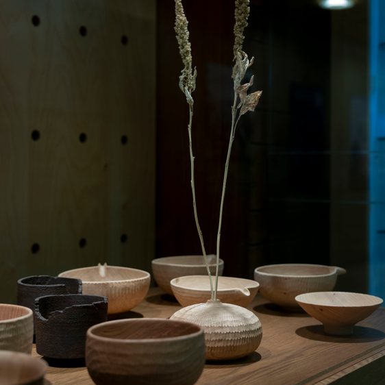Several carved wooden vessels and a vase holding dried flowers