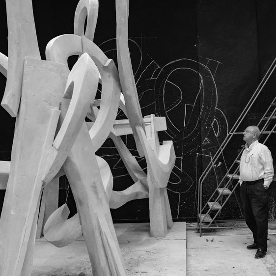 A man looks up at a large plaster sculpture made up of swooping interconnected sections in a gallery space.