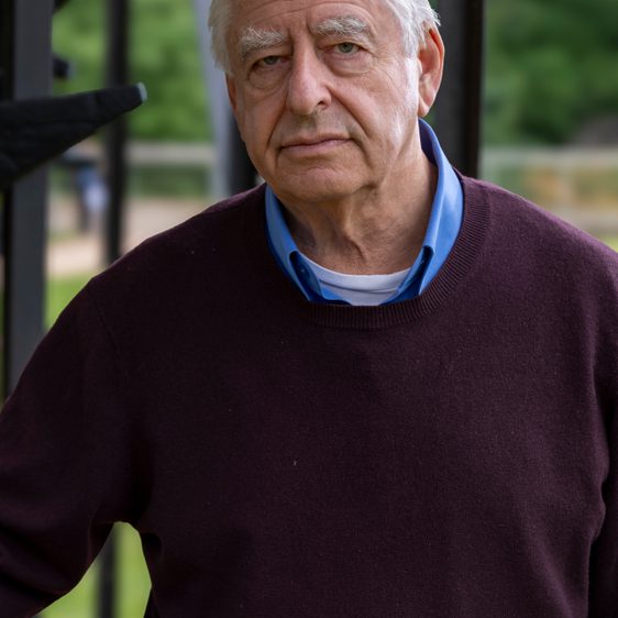 Portrait of a man with white hair, wearing a burgundy sweater and blue shirt.