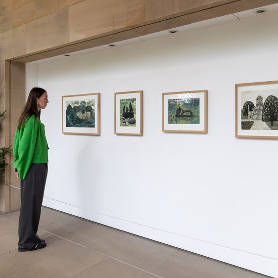 A woman in a green jumper looking at four framed prints on a white wall. A Christmas tree is at the left hand side.