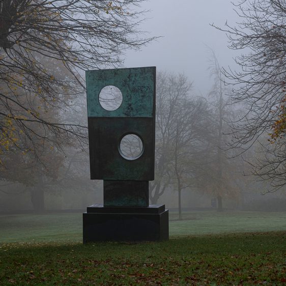 A rectangular sculpture with circular cut outs, displayed outdoors on a foggy day.