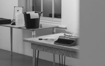 A black and white image of a studio set up with tables, typewriter and buckets.