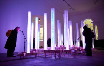 Two adults singing into microphones surrounded by glowing columns.