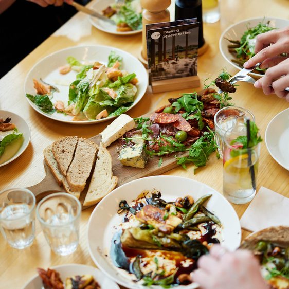 A table filled with small plates of food while hands holding forks reach for the food.