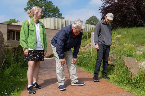 A group of three people looking at names embossed onto a metal walkway.