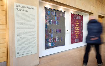 A person walking past a display of fabric banners with embroidered and appliquéd words.