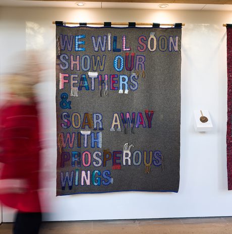 A person walking past a display of fabric banners with embroidered and appliquéd words.