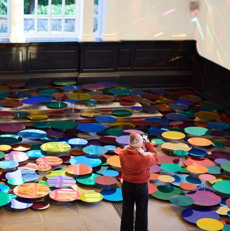 A woman in a winter coat taking a photo of an installation of colourful mirrored discs