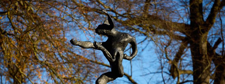 A sculpture of a hare balanced on the tip of an oversized anvil, displayed outdoors.