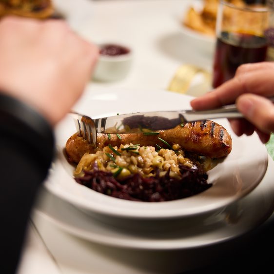 A person using cutlery to eat a plate of roasted meat and vegetables