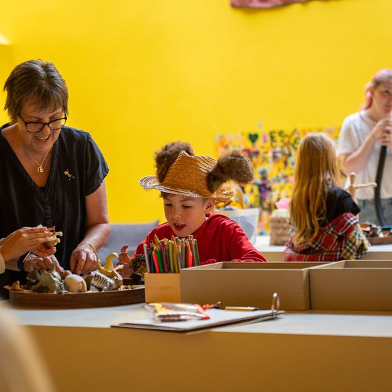 Families playing together in a yellow room with pencils and toy animals