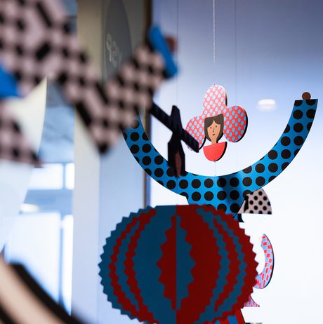 A series of colourful figurative mobiles displayed in a shop window.