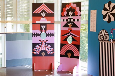 Two colourful patterned standees with holes for visitors to put their faces through. They are displayed in a bright room with a window behind them.