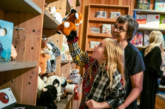 An adult and child picking up a fox soft toy from a shelf of products