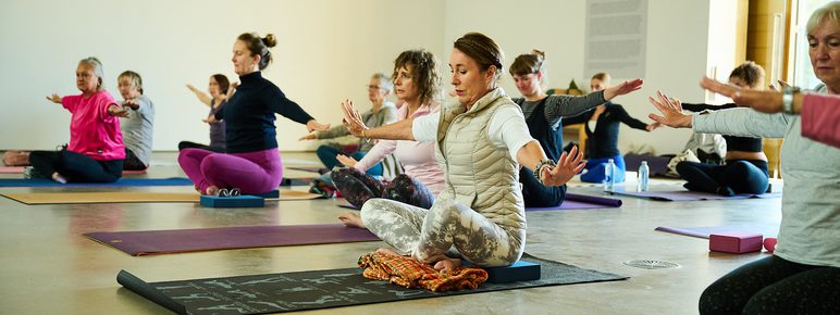 A group of people sitting on yoga mats and practicing yoga inside a gallery space.