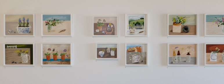 Rows of still life paintings displayed on a gallery wall.