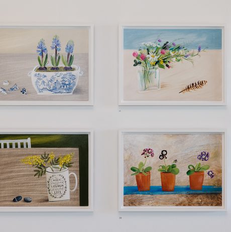 Four framed paintings of flowers in still life scenes, displayed in a grid on a gallery wall.