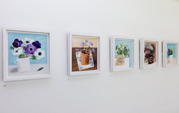 A row of frames paintings of flowers displayed on a gallery wall.