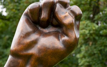 Detail of sculpture displayed outdoors showing a bronze fist.
