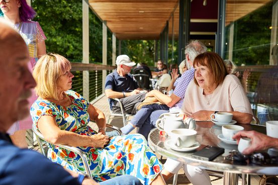 A couple of women sat chatting at a silver table over cake and tea.