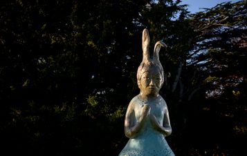 A sculpture of a figure with a rabbit head displayed outdoors.