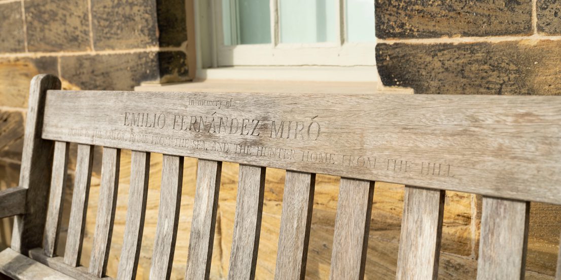 A close up of a wooden memorial bench with carved inscription.