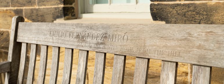 A close up of a wooden memorial bench with carved inscription.
