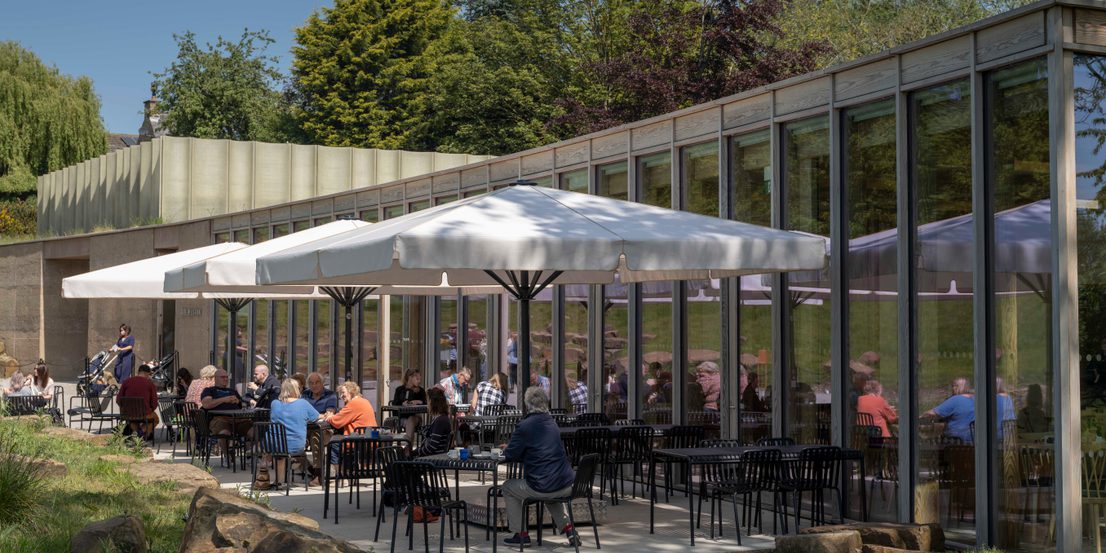 Groups of people eating at outdoor tables under sun umbrellas.