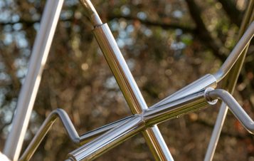 Close up of a metal mandala sculpture displayed outdoors. Trees are visible through the sculpture.